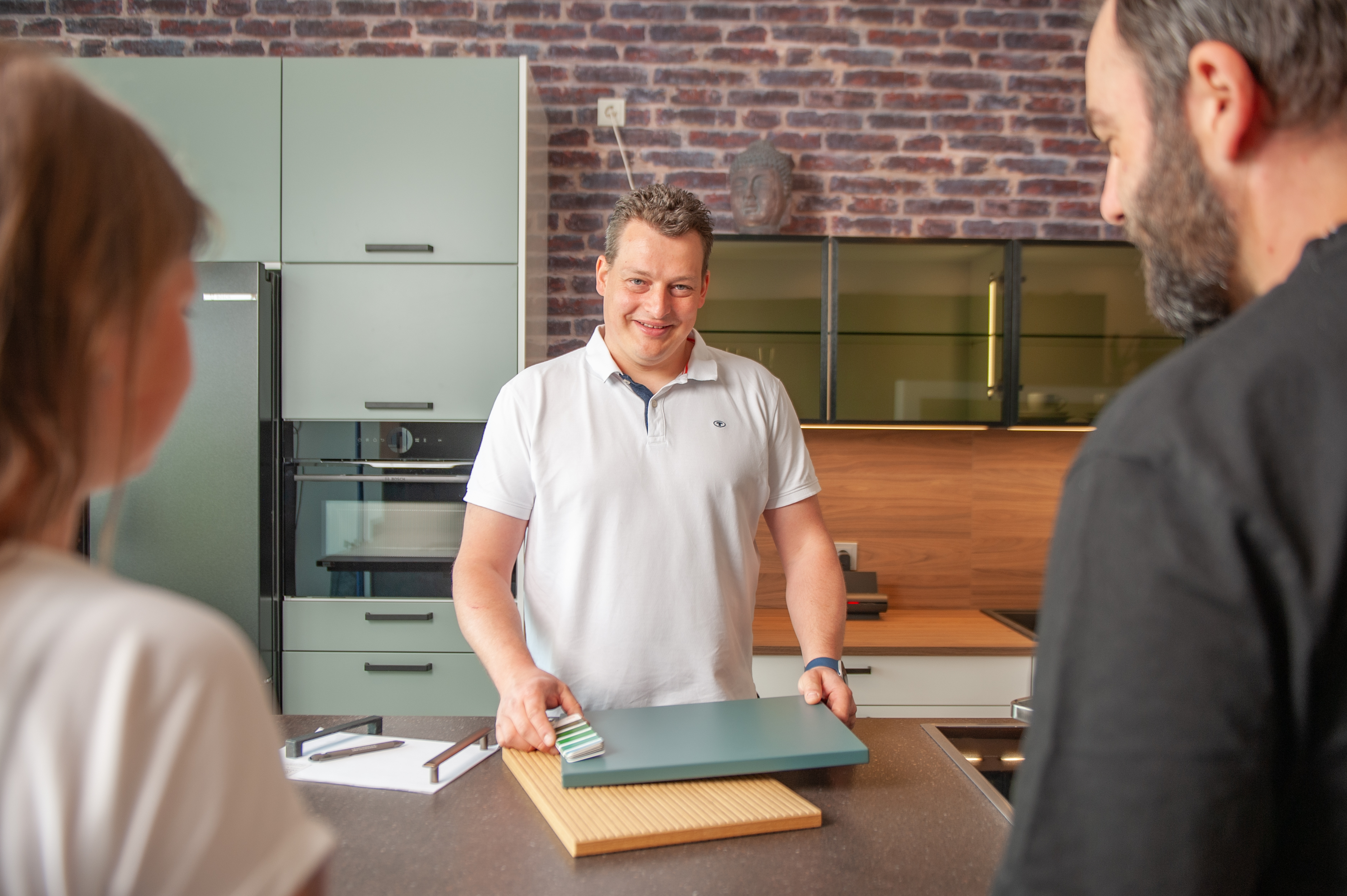 Florian Jacobi zeigt Küchenarbeitsplatte einem Paar in moderner Küche.