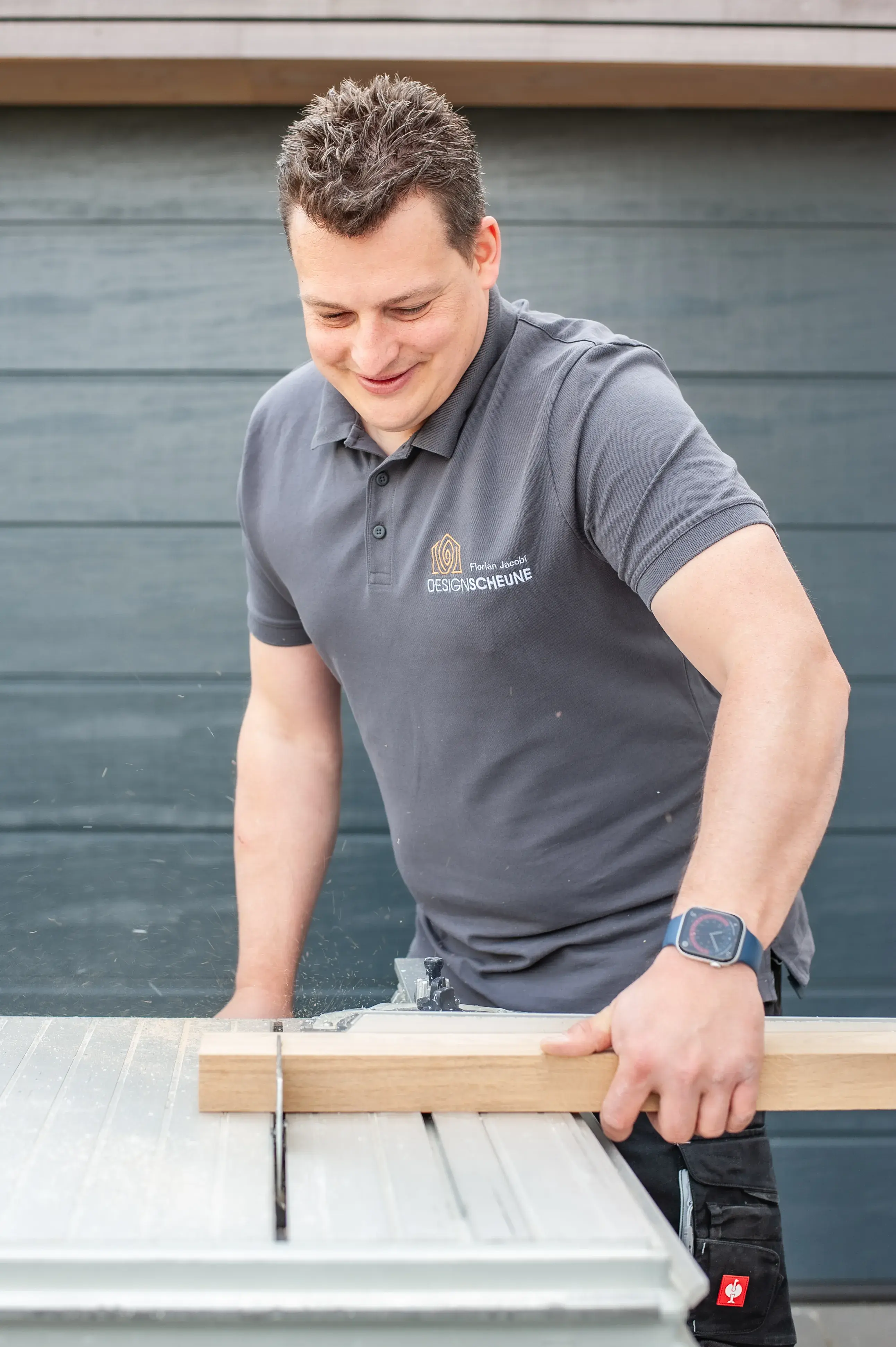 Florian Jacobi schneidet Holz mit einer Tischkreissäge und lächelt dabei.