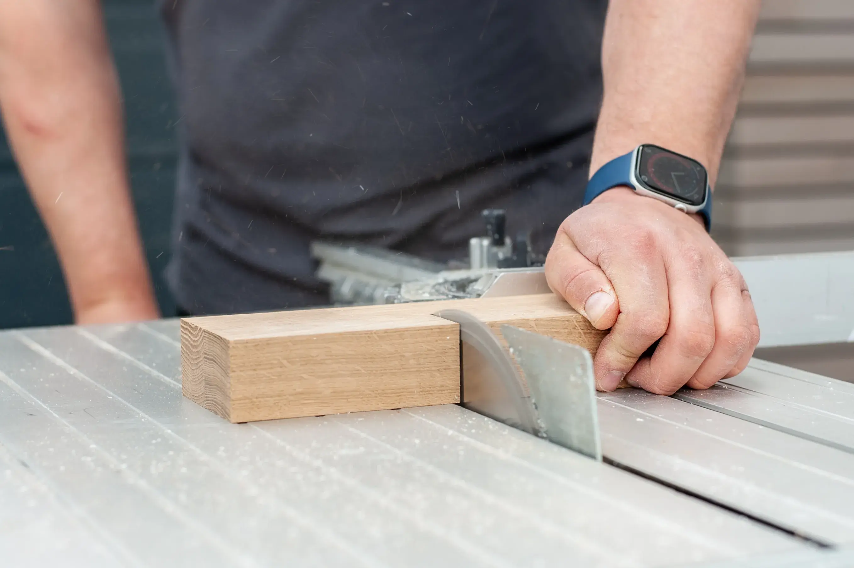 Hand führt Holz über eine Tischkreissäge zum Schneiden.