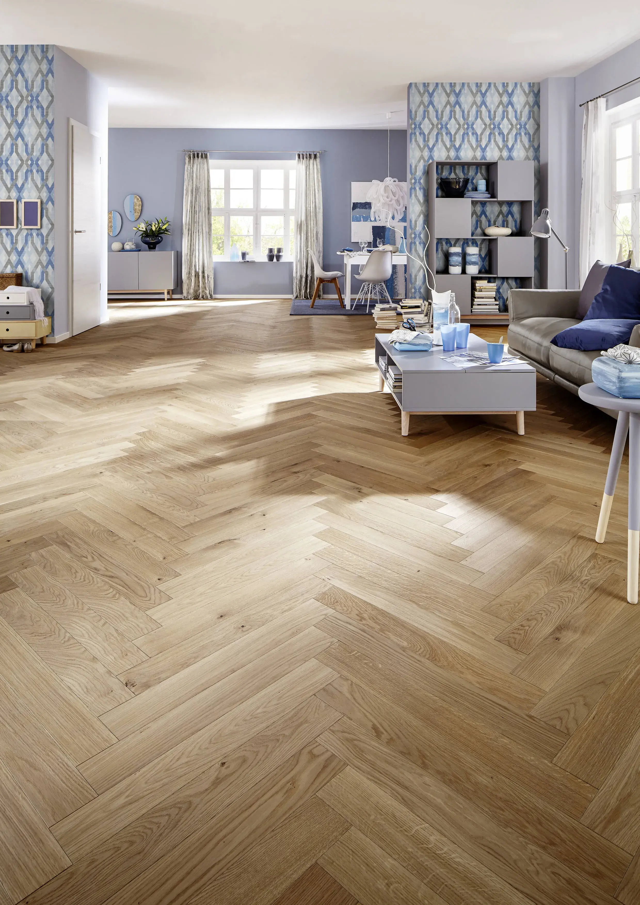 Helles Wohnzimmer mit Parkettboden, grauem Sofa und großen Fenstern.